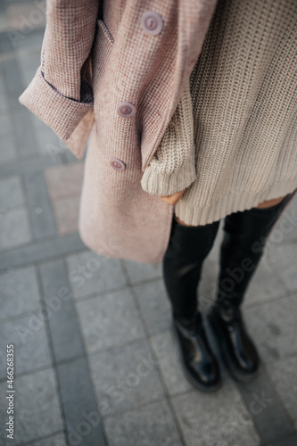 stylish image of urban fashion. knitted beige dress, pink delicate raincoat, black high boots on woman without face. autumn female look. cozy stily clothes. selective focus