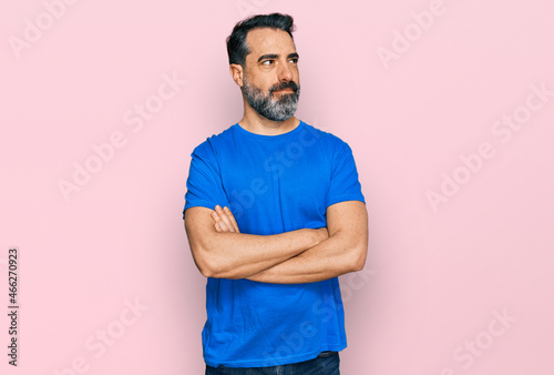 Middle aged man with beard wearing casual blue t shirt smiling looking to the side and staring away thinking.