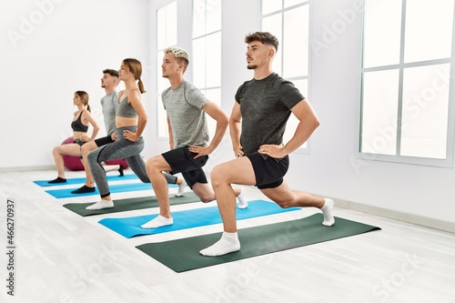 Group of young hispanic people concentrate training legs exercise at sport center.