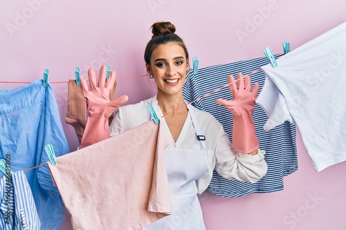 Beautiful brunette young woman washing clothes at clothesline showing and pointing up with fingers number ten while smiling confident and happy.