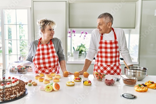Senior caucasian couple smiling happy baking sweets at the kitchen.
