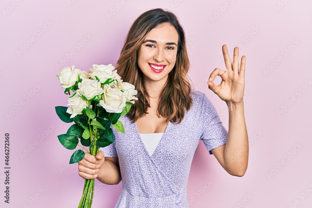 Young hispanic girl holding flowers doing ok sign with fingers, smiling friendly gesturing excellent symbol Young hispanic girl holding flowers doing ok sign with fingers, smiling friendly gesturing excellent symbol