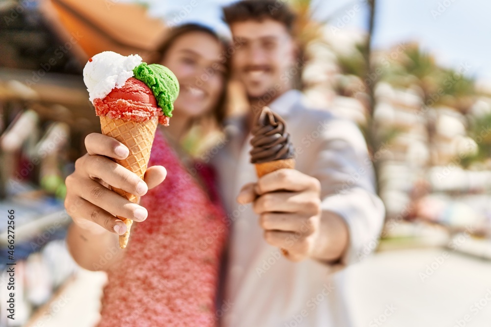 Young hispanic couple smiling happy eating ice cream standing at the city.
