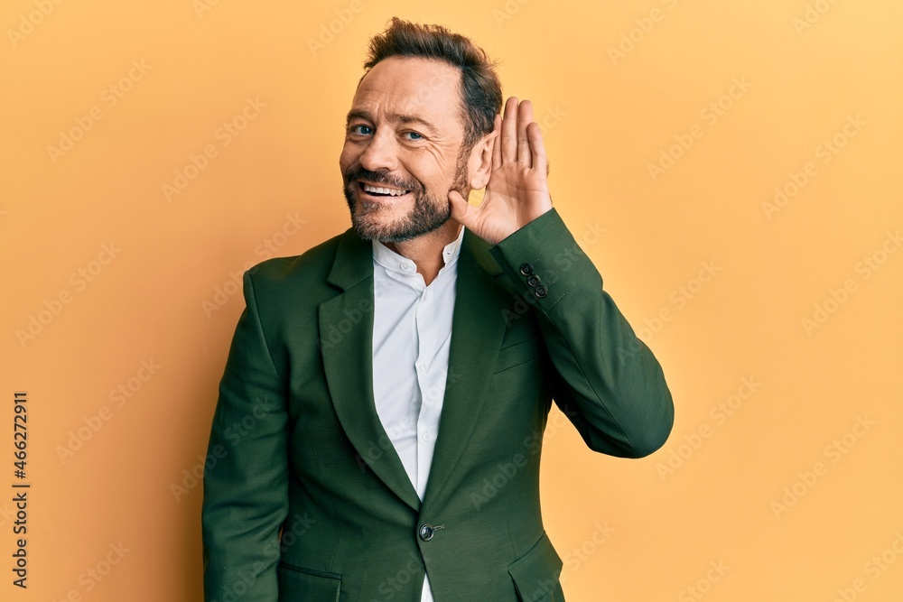 Middle age man wearing business suit smiling with hand over ear listening an hearing to rumor or gossip. deafness concept.