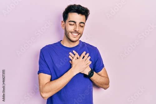 Young hispanic man wearing casual t shirt smiling with hands on chest with closed eyes and grateful gesture on face. health concept.