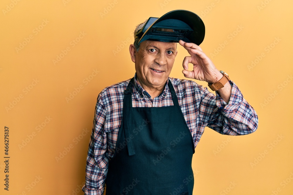 Handsome senior man with grey hair wearing welding protection mask smiling positive doing ok sign with hand and fingers. successful expression. Handsome senior man with grey hair wearing welding protection mask smiling positive doing ok sign with hand and fingers. successful expression.
