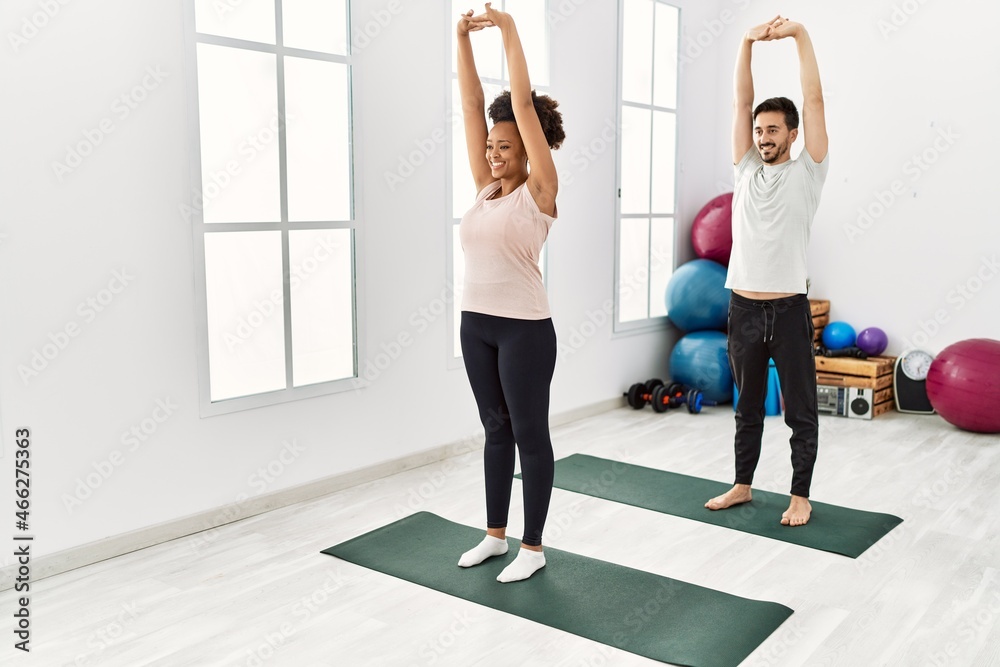 Fototapeta premium Young african american woman and hispanic man exercising at pilates room, stretching body and doing yoga pose, training strength and balance