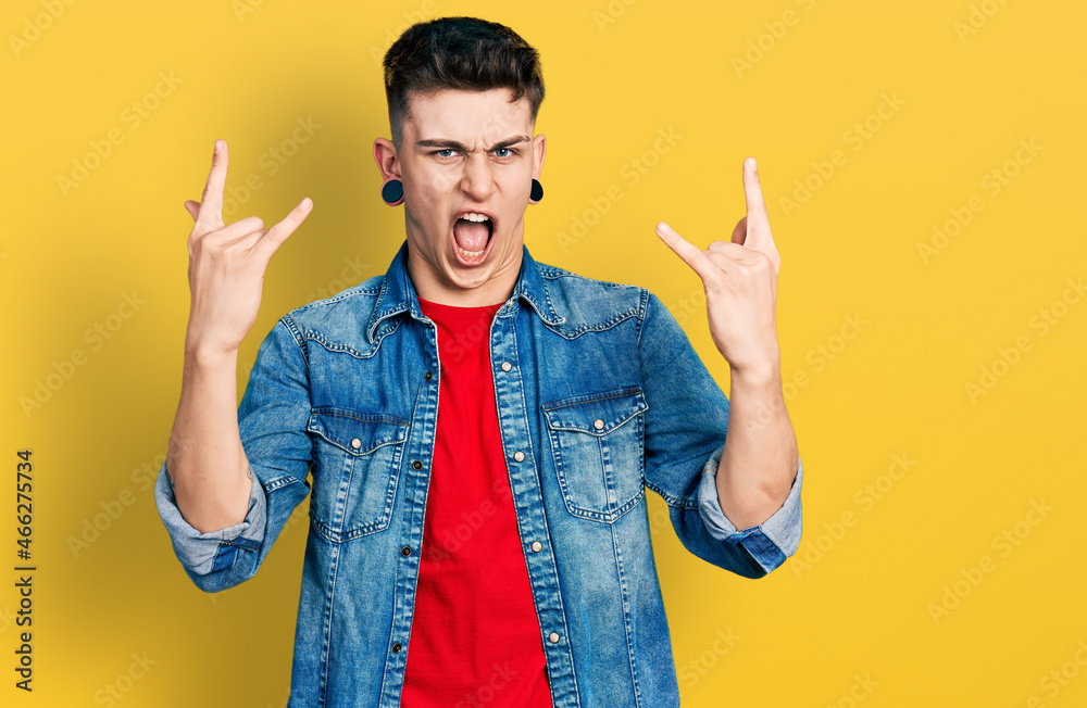 Young caucasian boy with ears dilation wearing casual denim jacket shouting with crazy expression doing rock symbol with hands up. music star. heavy concept. Young caucasian boy with ears dilation wearing casual denim jacket shouting with crazy expression doing rock symbol with hands up. music star. heavy concept.