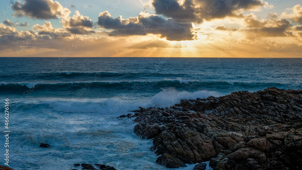 Light rays sunset with wave breaking on rocks