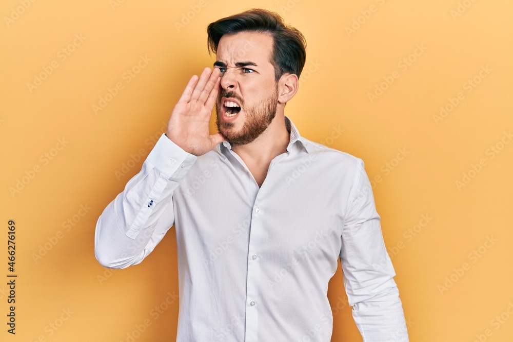 Handsome caucasian man with beard wearing business white shirt shouting and screaming loud to side with hand on mouth. communication concept. Handsome caucasian man with beard wearing business white shirt shouting and screaming loud to side with hand on mouth. communication concept.