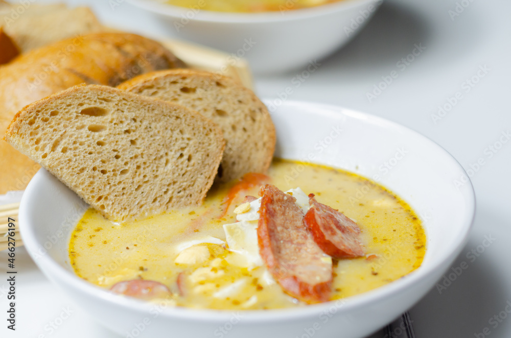 Traditional polish sour soup with sausage and eggs in ceramic bowl