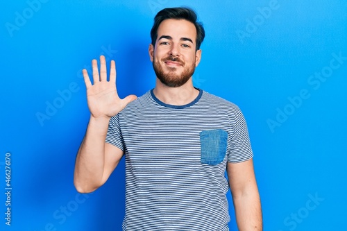 Handsome caucasian man with beard wearing casual striped t shirt showing and pointing up with fingers number five while smiling confident and happy.