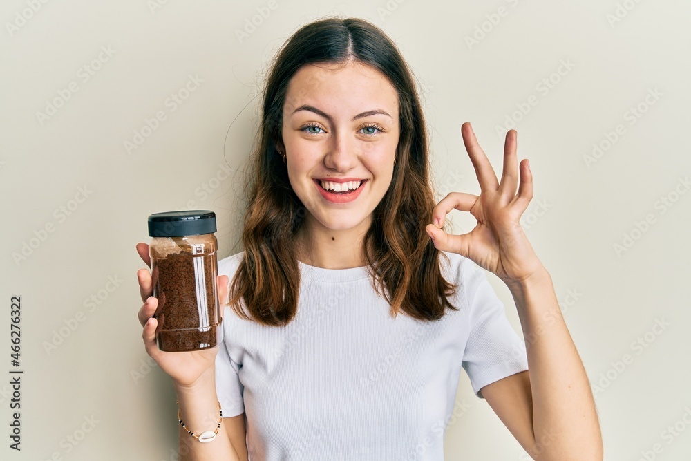 Young brunette woman holding soluble coffee doing ok sign with fingers, smiling friendly gesturing excellent symbol Young brunette woman holding soluble coffee doing ok sign with fingers, smiling friendly gesturing excellent symbol