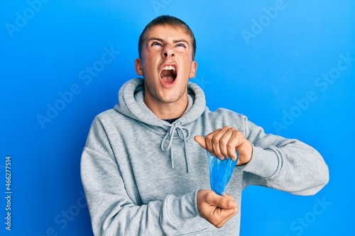 Young caucasian man holding slime angry and mad screaming frustrated and furious, shouting with anger looking up.