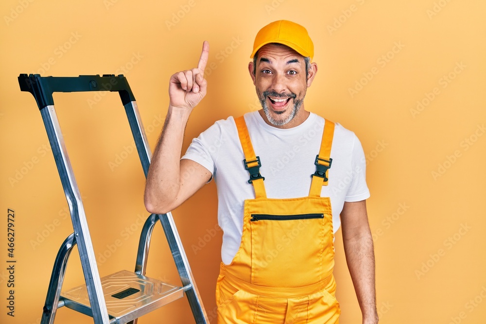 Handsome middle age man with grey hair holding ladder pointing finger up with successful idea. exited and happy. number one. Handsome middle age man with grey hair holding ladder pointing finger up with successful idea. exited and happy. number one.
