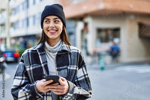 Young hispanic woman smiling happy using smartphone at the city.