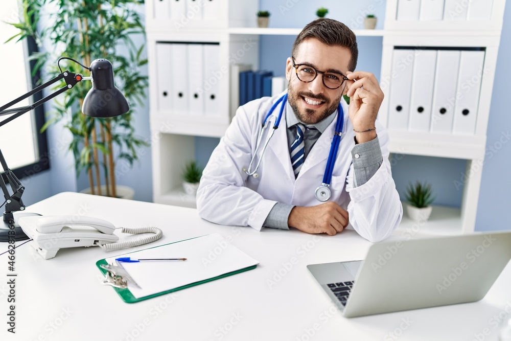 Young hispanic man wearing doctor uniform using laptop sitting at clinic Young hispanic man wearing doctor uniform using laptop sitting at clinic