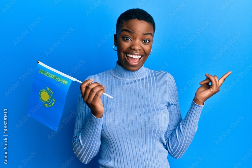 Young african american woman holding kazakhstan flag smiling happy pointing with hand and finger to the side Young african american woman holding kazakhstan flag smiling happy pointing with hand and finger to the side