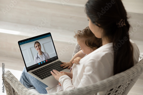 Loving mother hugging holding baby little daughter, using laptop, making video call to female pediatrician at home, doctor consulting caring mom online, telemedicine and children healthcare concept photo