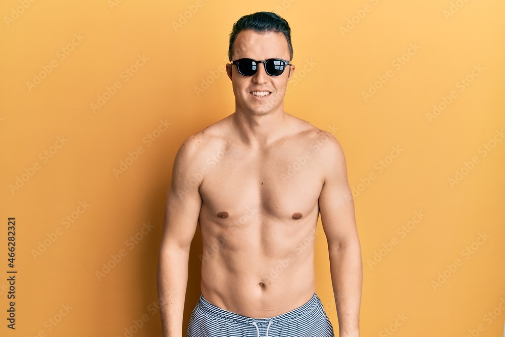 Handsome young man wearing swimsuit and sunglasses with a happy and cool smile on face. lucky person.