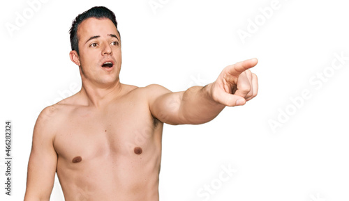 Handsome young man wearing swimwear shirtless pointing with finger surprised ahead, open mouth amazed expression, something on the front