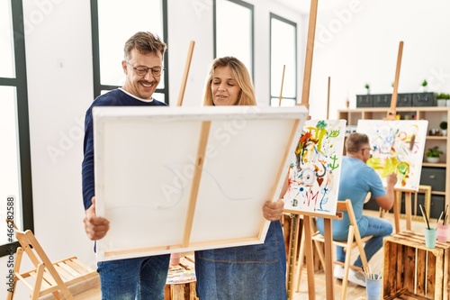 Group of middle age people drawing at art studio. Two students smiling happy holding canvas.