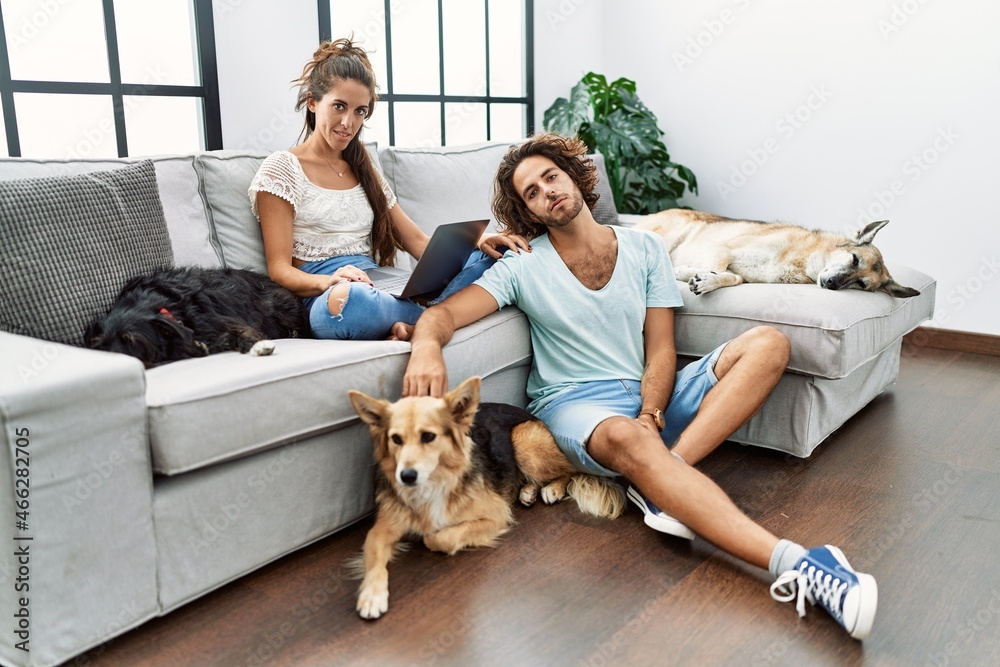 Young hispanic couple with dogs relaxing at home looking sleepy and tired, exhausted for fatigue and hangover, lazy eyes in the morning.