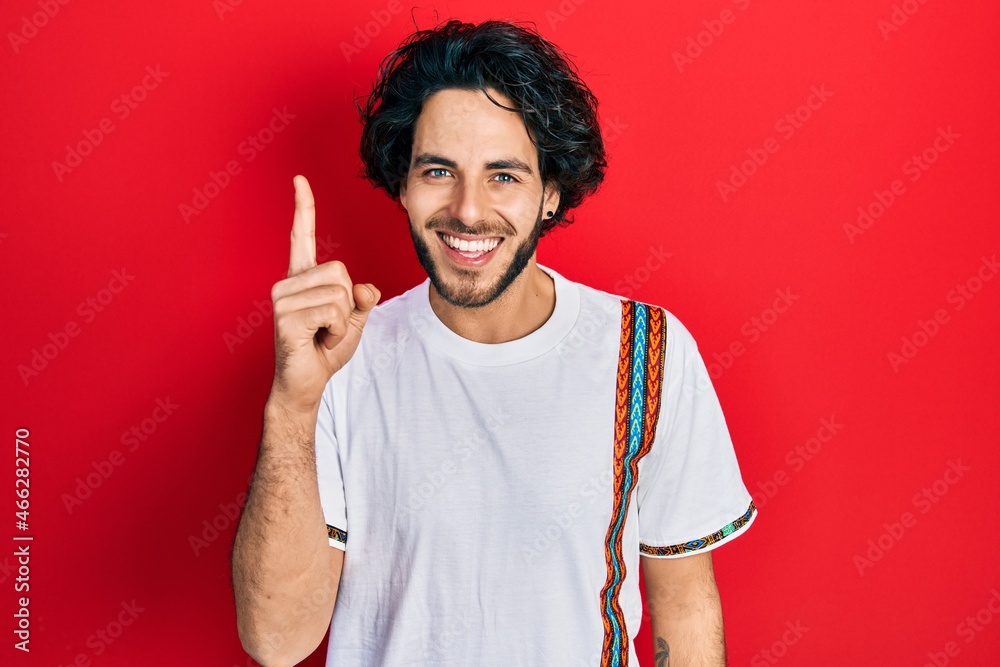 Handsome hispanic man wearing casual white t shirt pointing finger up with successful idea. exited and happy. number one. Handsome hispanic man wearing casual white t shirt pointing finger up with successful idea. exited and happy. number one.