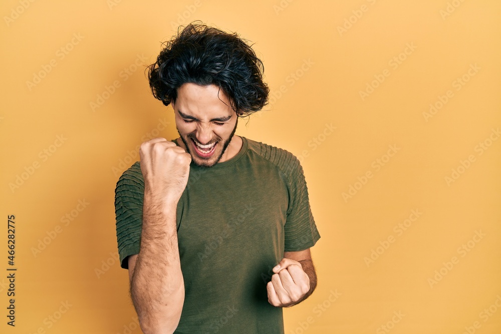 Handsome hispanic man wearing casual green t shirt celebrating surprised and amazed for success with arms raised and eyes closed Handsome hispanic man wearing casual green t shirt celebrating surprised and amazed for success with arms raised and eyes closed