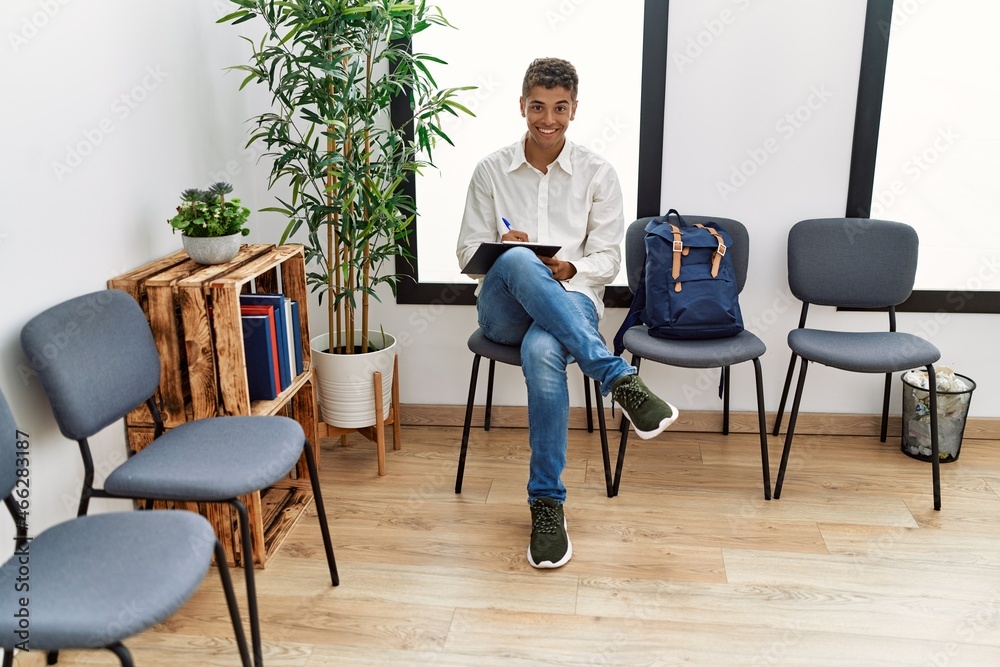 Young hispanic man waiting filling documents on clipboard at waiting room
