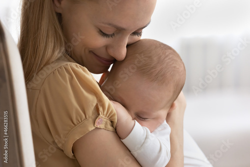 Close up loving young mother embracing holding cute sleeping baby on breast in arms, family enjoying tender moment, caring mom hugging newborn child infant, childhood and motherhood concept