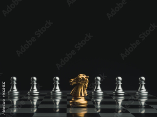 The golden horse, knight chess piece standing in front of silver pawn chess pieces on chessboard on dark background. Leadership, follower, team, commander, competition, and business strategy concept.