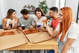 Group of young people smiling happy eating italian pizza sitting on the table at home