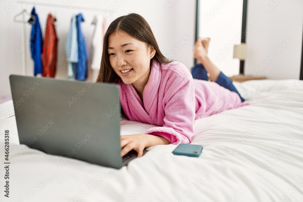 Young chinese girl using laptop lying on the bed at bedroom. Young chinese girl using laptop lying on the bed at bedroom.