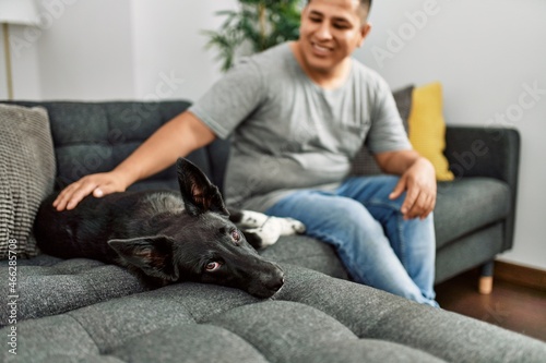 Young hispanic man smiling happy sitting on the sofa with dog at home. © Krakenimages.com