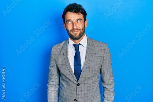 Handsome man with beard wearing business suit and tie smiling looking to the side and staring away thinking.