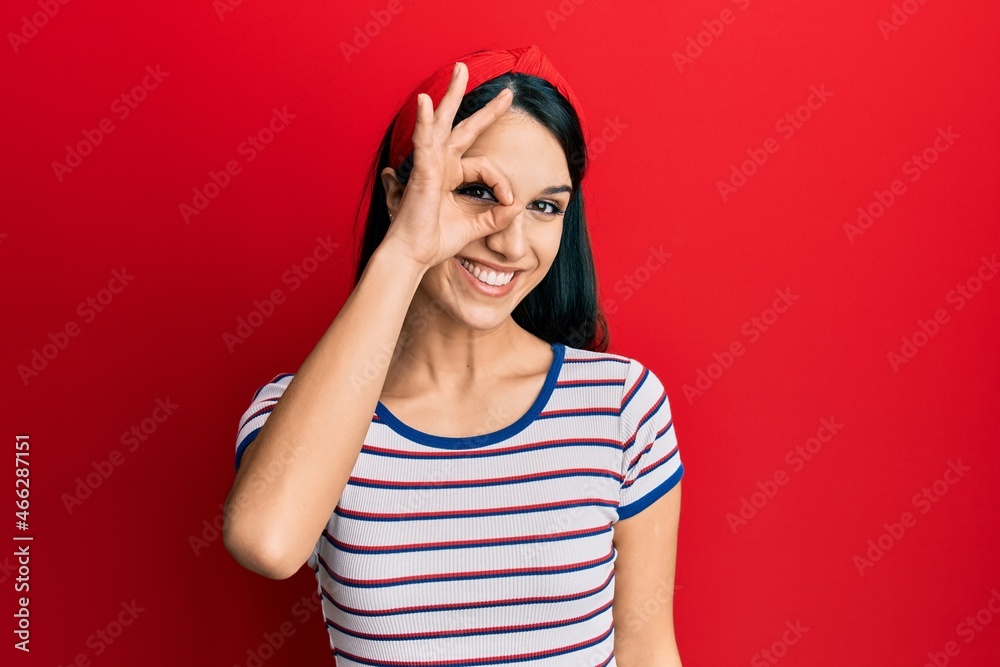 Young hispanic woman wearing casual clothes smiling happy doing ok sign with hand on eye looking through fingers