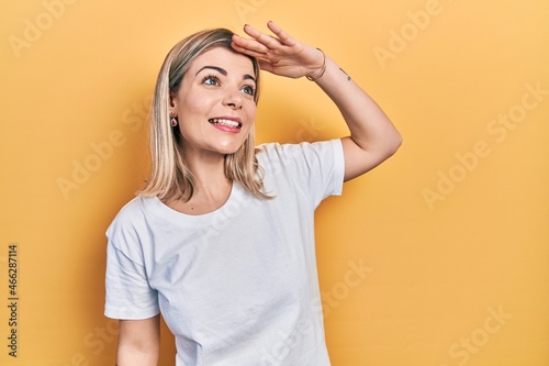 Beautiful caucasian woman wearing casual white t shirt very happy and smiling looking far away with hand over head. searching concept.