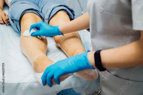 A master or cosmetologist in blue gloves rubs the client's feet, preparing for the epilation procedure.