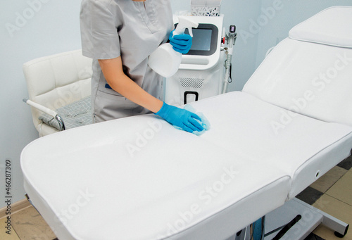 A master or cosmetologist in blue gloves wipes the workplace with an antiseptic  preparing for the epilation procedure.