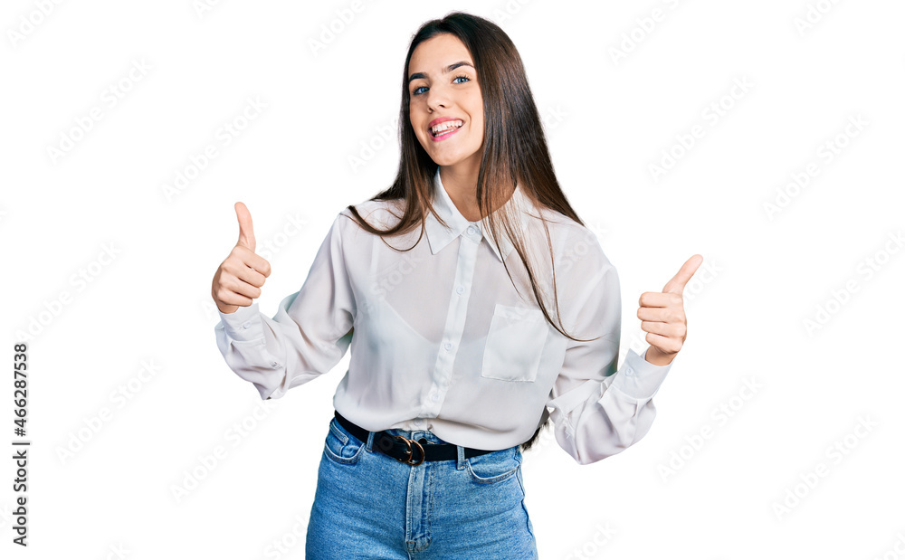 Young brunette teenager wearing business white shirt success sign doing positive gesture with hand, thumbs up smiling and happy. cheerful expression and winner gesture.