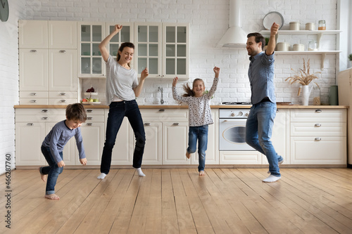 Full length happy young couple parents dancing to energetic disco music with smiling little children son daughter in modern kitchen, having fun together at home, enjoying active carefree weekend time. © fizkes