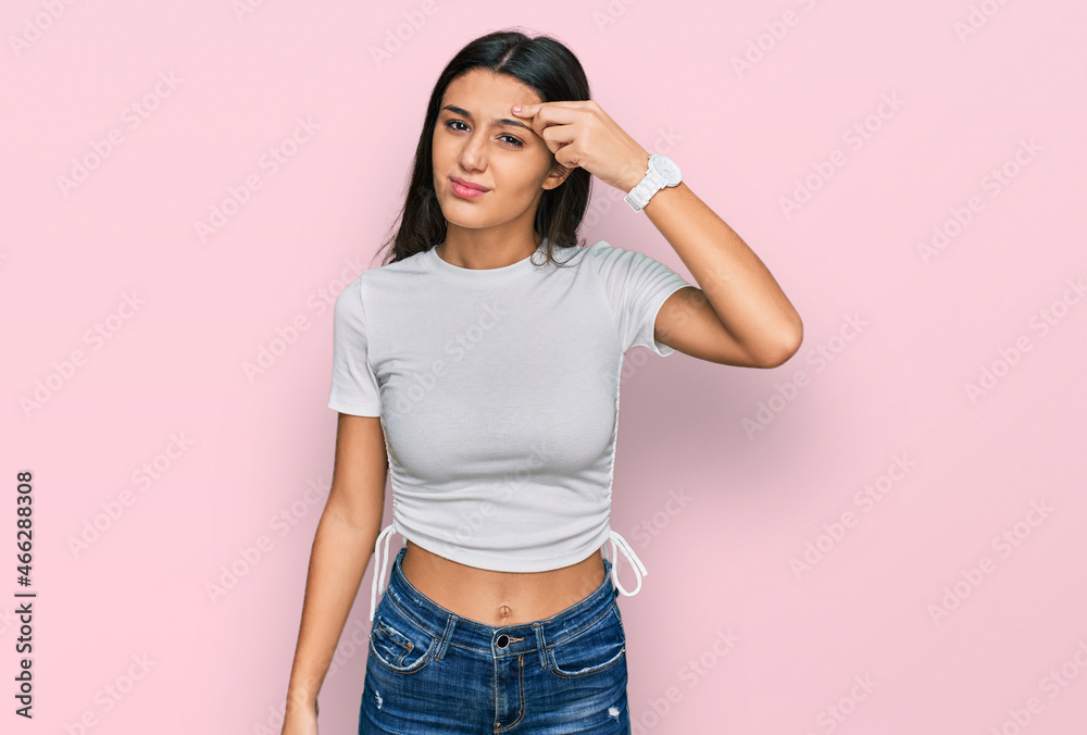 Young hispanic girl wearing casual white t shirt pointing unhappy to pimple on forehead, ugly infection of blackhead. acne and skin problem Young hispanic girl wearing casual white t shirt pointing unhappy to pimple on forehead, ugly infection of blackhead. acne and skin problem