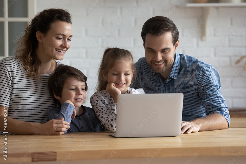 Happy caring young couple parents watching funny cartoons or photo video content in social networks with little cute children siblings on computer, choosing goods shopping together in internet store. Happy caring young couple parents watching funny cartoons or photo video content in social networks with little cute children siblings on computer, choosing goods shopping together in internet store.