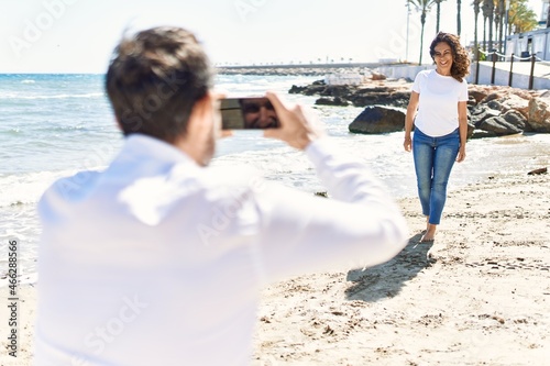 Middle age hispanic man make photo by the smartphone to woman at the beach.