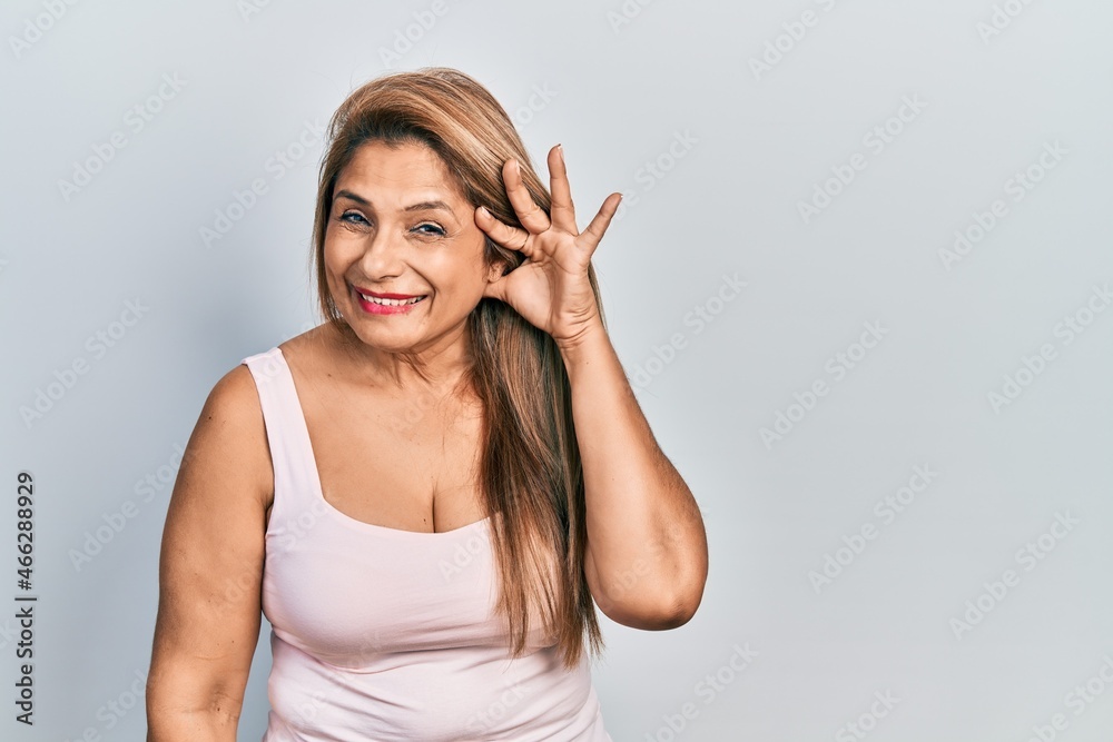 Fototapeta premium Middle age hispanic woman wearing casual style with sleeveless shirt smiling with hand over ear listening an hearing to rumor or gossip. deafness concept.