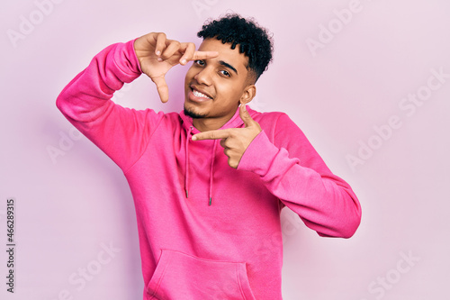 Young african american man wearing casual sweatshirt smiling making frame with hands and fingers with happy face. creativity and photography concept.
