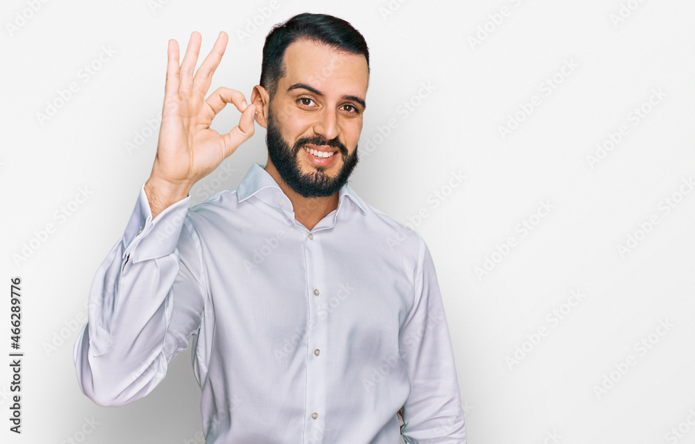 Young man with beard wearing business shirt smiling positive doing ok sign with hand and fingers. successful expression. Young man with beard wearing business shirt smiling positive doing ok sign with hand and fingers. successful expression.