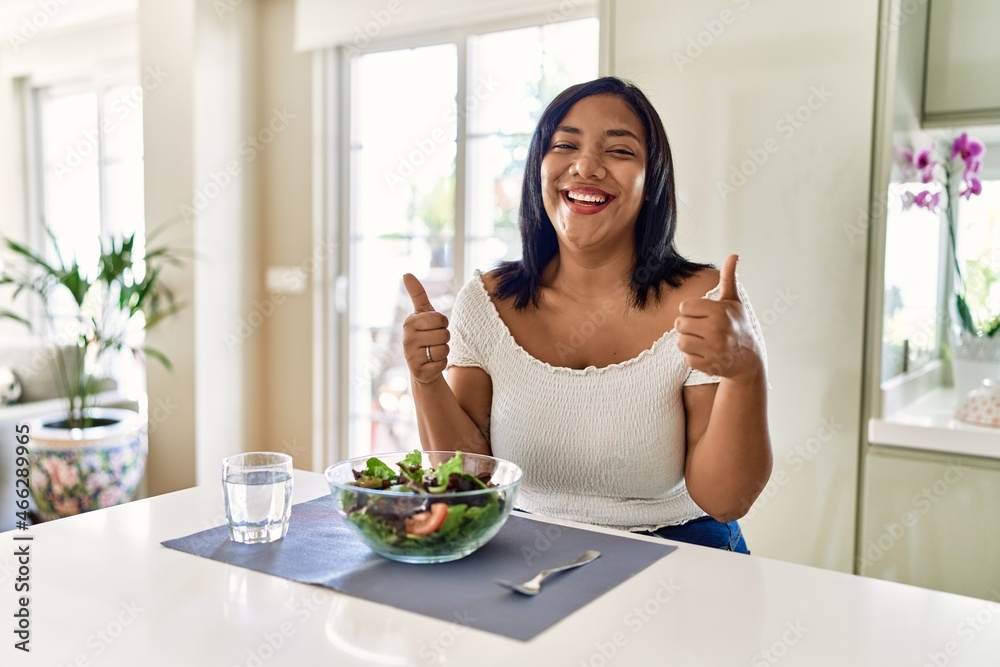 Young hispanic woman eating healthy salad at home success sign doing positive gesture with hand, thumbs up smiling and happy. cheerful expression and winner gesture. Young hispanic woman eating healthy salad at home success sign doing positive gesture with hand, thumbs up smiling and happy. cheerful expression and winner gesture.
