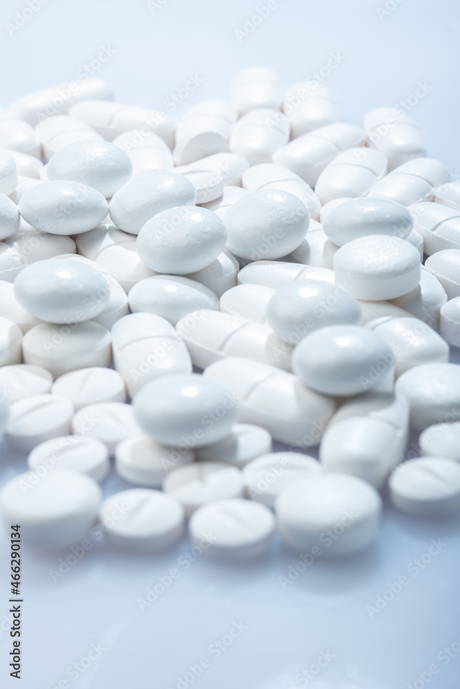 Closeup of white pills against white background. White pill container in the background.